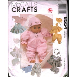 May include: McCall's Crafts pattern envelope 8554 featuring illustrations of doll clothing including a pink romper and hat, a blue dress, a yellow top and pants, a floral top and pants, and various bonnets, all labeled with letters A through L.