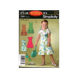 May include: Simplicity sewing pattern 2991 for a dress in sizes 3, 4, 5, 7, and 8. The envelope features illustrations of various dress styles, including a green floral print, a solid pink dress, and a plaid dress, alongside a green circular bag.