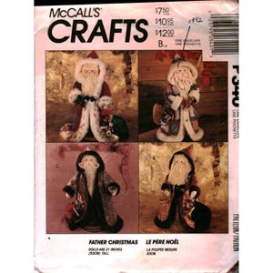 Op de afbeelding: McCall's Crafts patroon voor kerstmanpoppen, 53cm hoog. Het patroon toont verschillende poppenontwerpen met rode en witte outfits, lange witte baarden en tassen. De tekst "ONE ENVELOPE UNE POCHETTE" is inbegrepen.