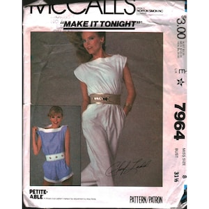 May include: A white ceramic mug with a black handle and the text "But First, Coffee" in a bold, black font. The mug is set against a blurred background, suggesting a cozy setting.