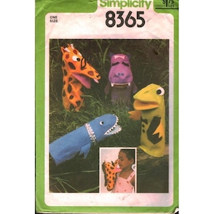 May include: Simplicity pattern 8365 featuring various animal hand puppets. The puppets include a giraffe, hippo, shark, and a yellow creature. The pattern cover has a green border and the text "ONE SIZE".
