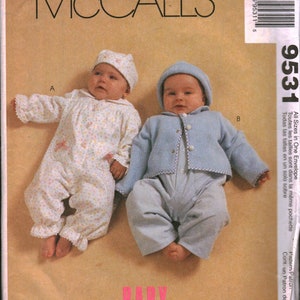 Peut inclure: Un patron de couture pour vêtements de bébé, présentant deux tenues pour bébé. La première tenue est un body blanc à imprimé floral rose avec un bonnet blanc. La deuxième tenue est un body bleu clair avec un col blanc et un bonnet bleu clair. Le patron s'appelle "McCall's 9531 Baby Wear".