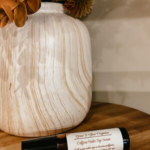K&ouml;nnte beinhalten: Eine braune Glasrollflasche mit einem wei&szlig;en Etikett, auf dem "Grow & Glow Organics Caffeine Under Eye Serum" steht. Das Etikett enth&auml;lt auch Gebrauchsanweisungen: "Serum unter die Augen rollen, um Schwellungen und Augenringe zu reduzieren - direkten Kontakt mit den Augen vermeiden".