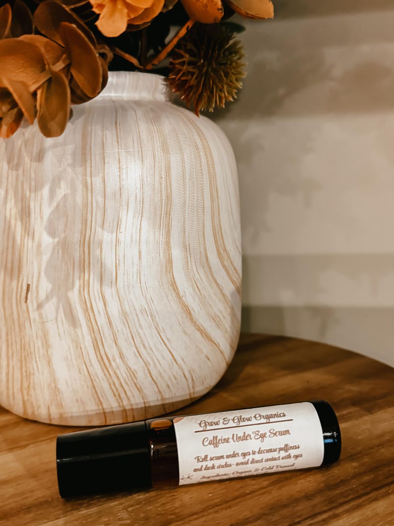 K&ouml;nnte beinhalten: Eine braune Glasrollflasche mit einem wei&szlig;en Etikett, auf dem "Grow & Glow Organics Caffeine Under Eye Serum" steht. Das Etikett enth&auml;lt auch Gebrauchsanweisungen: "Serum unter die Augen rollen, um Schwellungen und Augenringe zu reduzieren - direkten Kontakt mit den Augen vermeiden".