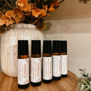 May include: Five amber glass roller bottles with labels for essential oil blends. The labels are white with black text and feature names like "Mighty Night", "Tiny Tummy", and "Little Sickly".