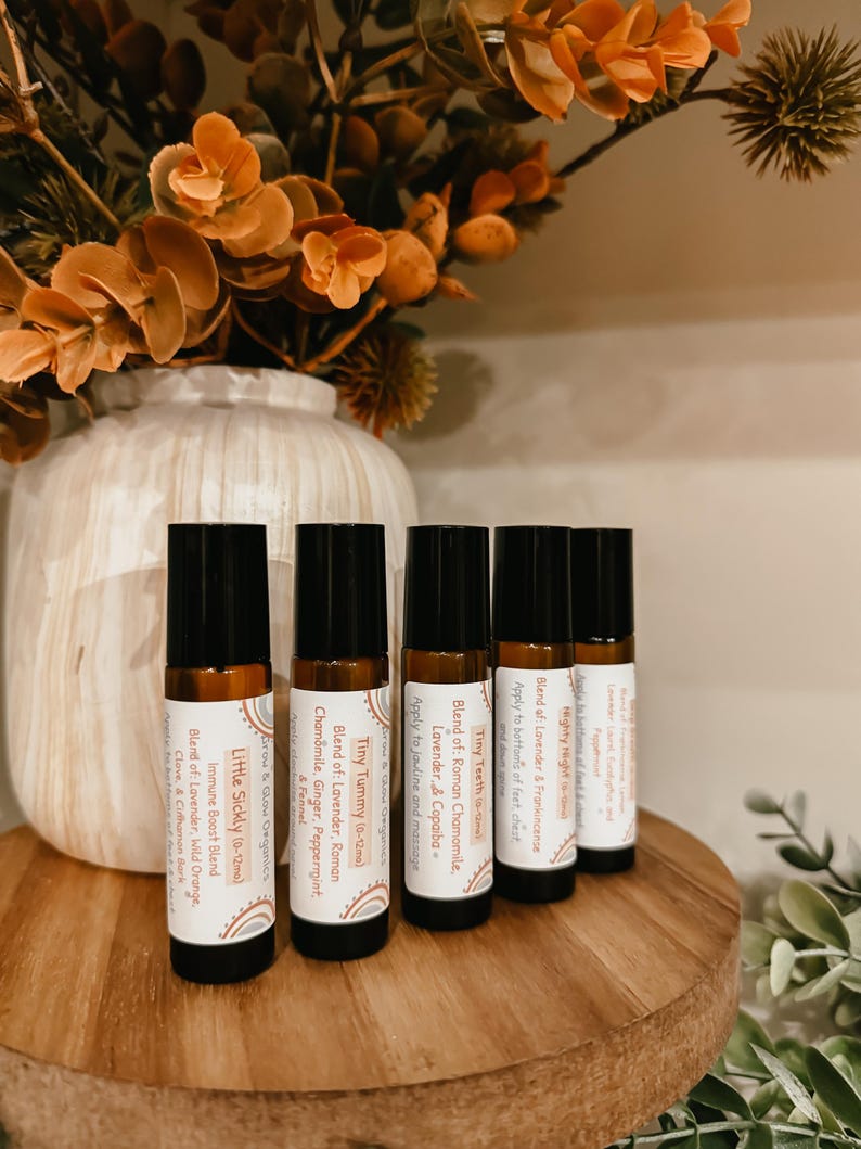 May include: Five amber glass roller bottles with labels for essential oil blends. The labels are white with black text and feature names like "Mighty Night", "Tiny Tummy", and "Little Sickly".
