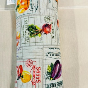 May include: A rectangular pillow with a white background and a pattern of vegetable labels. The labels feature illustrations of pumpkins, beets, eggplants, and peppers. The text includes "Vegetables", "Garden Seeds", and "Farmers Market".