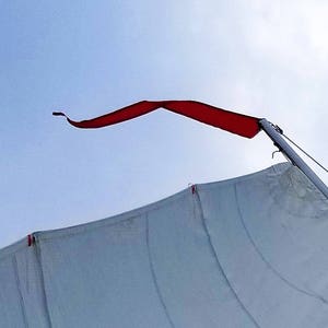 May include: A white sail billowing in the wind with a red flag attached to the mast. The sail is partially unfurled and the flag is flowing in the breeze.