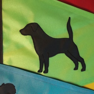 以下が含まれることがあります： 緑の布地に黒い犬のシルエットが刺繍された旗。旗は青い布地の旗の上に折り畳まれている。
