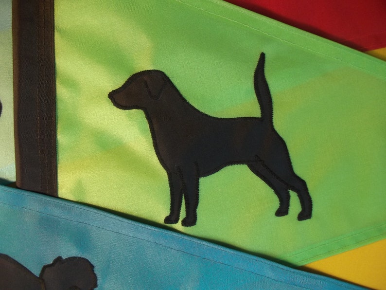 以下が含まれることがあります： 緑の布地に黒い犬のシルエットが刺繍された旗。旗は青い布地の旗の上に折り畳まれている。