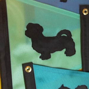 以下が含まれることがあります： 黒色の犬のシルエットが描かれた緑と青の布製の旗。旗は黒い縁取りと金色のハトメが付いています。