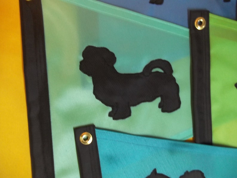 以下が含まれることがあります： 黒色の犬のシルエットが描かれた緑と青の布製の旗。旗は黒い縁取りと金色のハトメが付いています。