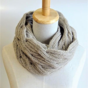May include: A beige knitted infinity scarf with a cable knit pattern.