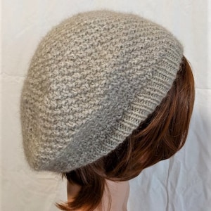 May include: A light gray knitted beret with a textured stitch pattern. The beret is worn on a mannequin with brown hair.