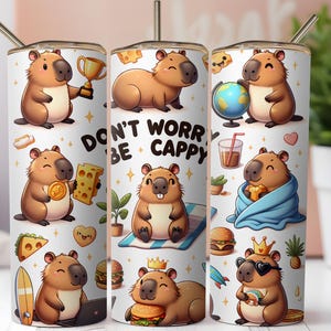 May include: A white tumbler featuring cartoon capybaras with various accessories and the text "DON'T WORRY BE CAPPY." The capybaras are depicted with a trophy, cheese, a globe, and other items. The tumbler has a silver straw.