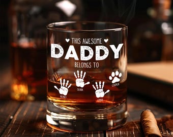 May include: A personalized rocks glass with the text "THIS AWESOME DADDY BELONGS TO" and handprints and a paw print. The glass is filled with amber liquid and sits on a wooden surface with a cigar.