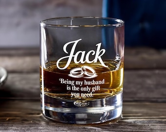 May include: A clear glass tumbler with a golden liquid inside. The word "Jack" is written in elegant script, with the phrase "Being my husband is the only gift you need" below it. Two wedding rings are also featured.