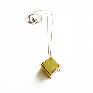 May include: A gold necklace with a geometric pendant. The pendant is a cube with a square face and is made of brass. The necklace is on a white background.