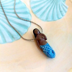 May include: A silver chain necklace with a blue and white mermaid pendant. The mermaid is brown-skinned and has long black hair.