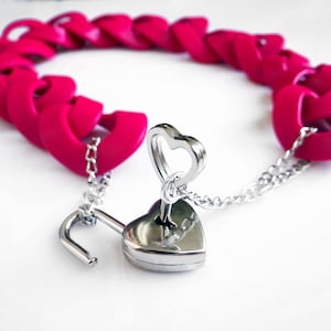 May include: A pink heart-shaped chain bracelet with a silver heart-shaped padlock and key.