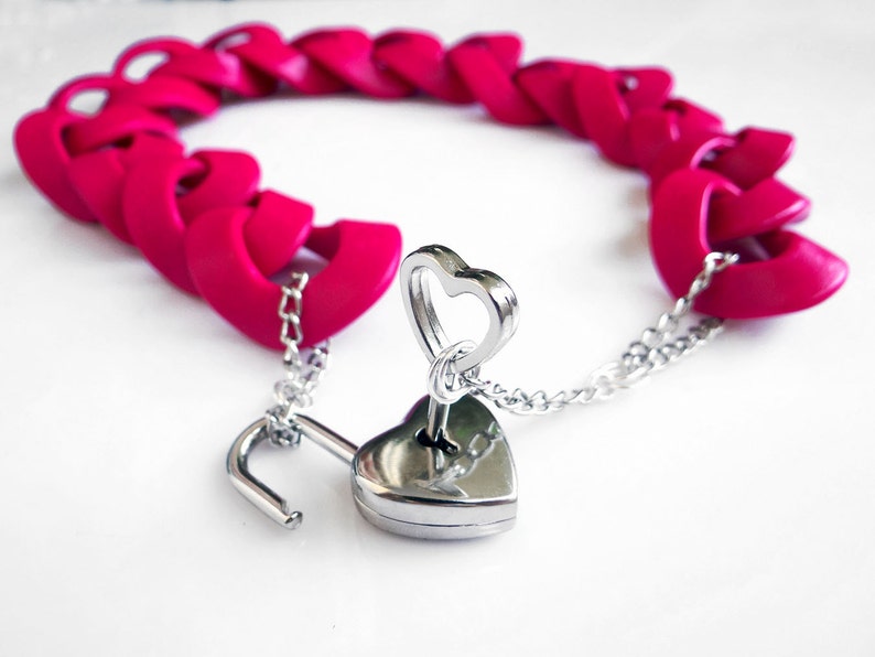 May include: A pink heart-shaped chain bracelet with a silver heart-shaped padlock and key.