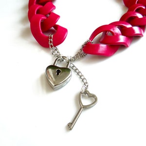 May include: A pink plastic chain necklace with a heart-shaped padlock and key. The necklace is made of interlocking heart-shaped links.