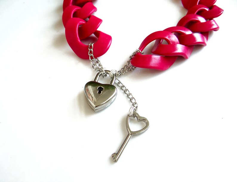 May include: A pink plastic chain necklace with a heart-shaped padlock and key. The necklace is made of interlocking heart-shaped links.