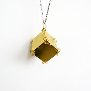 May include: A gold-toned necklace with a geometric pendant made of multiple brass squares. The pendant is a cube shape with a chain attached to the top.
