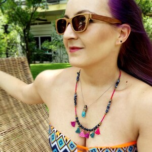 May include: A woman wearing a colourful bikini top with a layered necklace featuring blue and black beads, a small pendant, and pink and turquoise tassels.