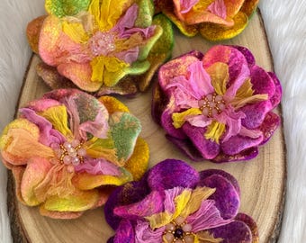 May include: Five felt flower brooches in shades of pink, yellow, green, and purple. Each flower has a centre of pink and yellow fabric with beaded accents.