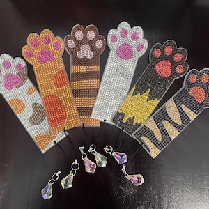 May include: Seven colourful paw print bookmarks with rhinestones. Each bookmark has a different design and colour scheme. The bookmarks are attached to silver chains with crystal charms.