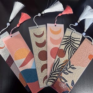 May include: Five different bookmark designs featuring pink, orange, brown and white geometric patterns. Each bookmark has a white tassel attached.