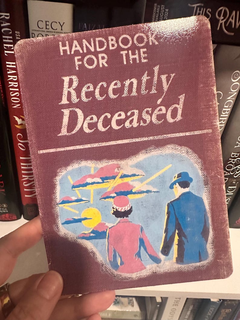 Puede incluir: Una portada de libro de estilo vintage con el t&iacute;tulo "Handbook for the Recently Deceased" en letras blancas sobre un fondo granate. La portada presenta una ilustraci&oacute;n de dos figuras en un paisaje surrealista.