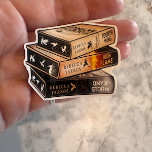 Op de afbeelding: Een sticker met een stapel van drie boeken met de titels "Fourth Wing", "Iron Flame" en "Onyx Storm" van Rebecca Yarros. De boeken hebben een fantasiethema met decoratieve elementen en een witte rand.