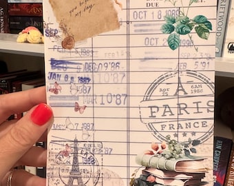 Peut inclure: Un papier décoratif avec un design de carte de bibliothèque vintage. Il présente des illustrations florales, des papillons et le texte "you brighten my day". Le design comprend un tampon de Paris, France, et une pile de livres.