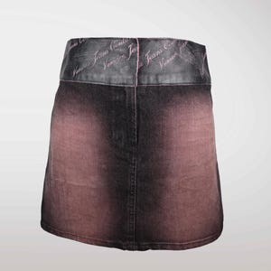 May include: A denim skirt with a faded, ombre effect in shades of black and reddish-brown. The waistband is a darker material with the text "Versace Jeans Couture" in a cursive font.