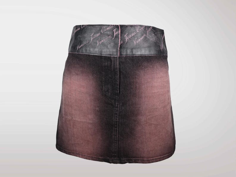 May include: A denim skirt with a faded, ombre effect in shades of black and reddish-brown. The waistband is a darker material with the text "Versace Jeans Couture" in a cursive font.