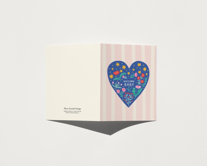 Puede incluir: Tarjeta de felicitaci&oacute;n con un dise&ntilde;o de coraz&oacute;n azul con flores y las palabras "Welcome Baby". El coraz&oacute;n est&aacute; sobre un fondo de rayas rosas y blancas. El lado izquierdo de la tarjeta es de color crema s&oacute;lido.