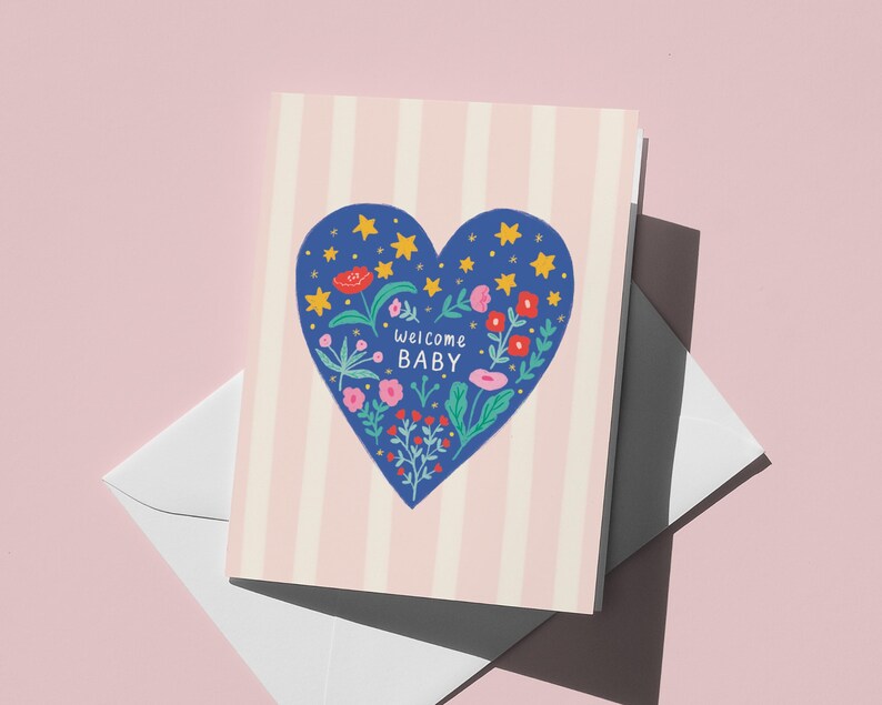 Puede incluir: Una tarjeta de felicitaci&oacute;n con un dise&ntilde;o de coraz&oacute;n azul lleno de flores y estrellas, con las palabras "Welcome Baby" en su interior. La tarjeta tiene un fondo a rayas rosas y blancas y va acompa&ntilde;ada de un sobre blanco.