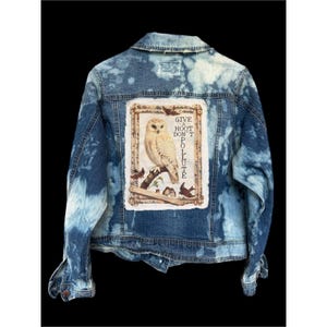 May include: A blue denim jacket with a bleached tie-dye pattern featuring a rectangular patch on the back. The patch displays a detailed illustration of an owl perched on a branch with the text "GIVE A HOOT DON'T POLLUTE" and small birds.
