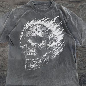 May include: A gray t-shirt featuring a white graphic of a skull engulfed in flames. The shirt has a crew neck and short sleeves. The text "OLD SCHOOL CURIOS" is printed in white at the bottom right.