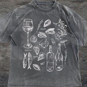 May include: A gray t-shirt featuring a white illustration of seafood and wine. The design includes a wine glass, bottles, oysters, mussels, sardines, and grapes. The text "Old School Curios" is at the bottom right.