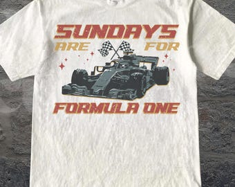 Puede incluir: Camiseta blanca con un gráfico de un coche de carreras de Fórmula 1. El texto "SUNDAYS ARE FOR FORMULA ONE" está en rojo y dorado. El diseño incluye banderas a cuadros y estrellas. Cuello redondo.