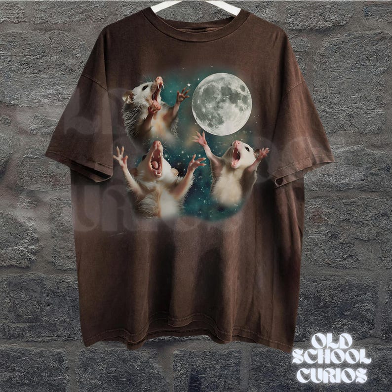 May include: Brown t-shirt featuring a graphic of three opossums howling at a full moon. The opossums are white and gray, with their mouths open. The moon is large and detailed. The shirt has a vintage, distressed look.