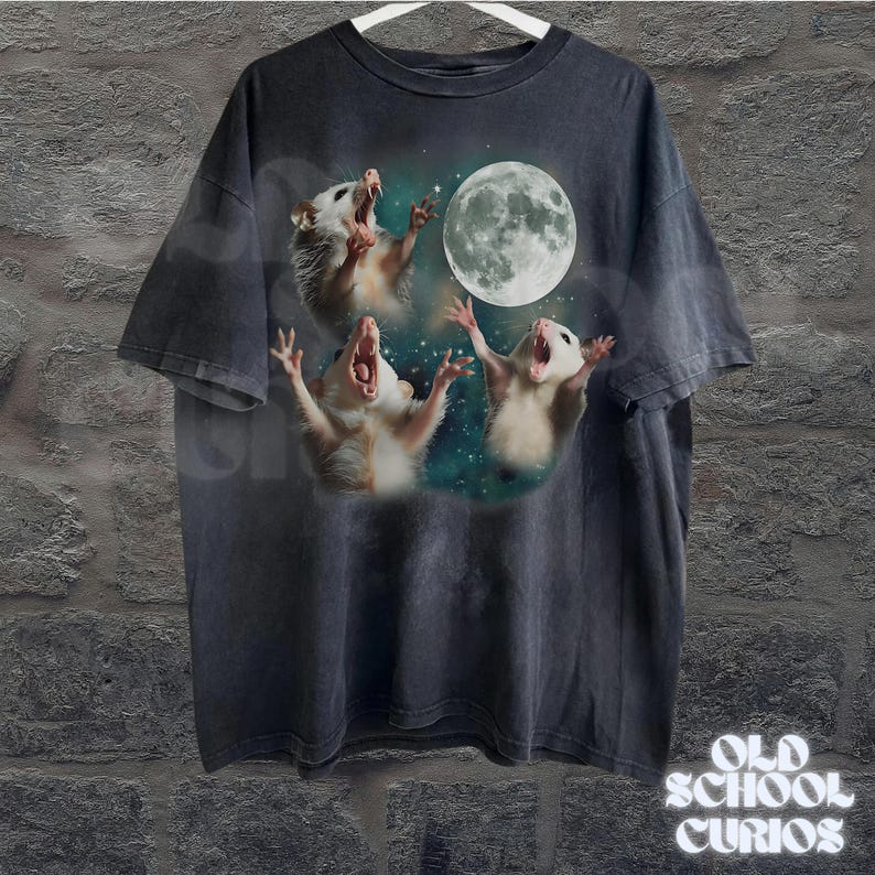 May include: Dark gray t-shirt featuring a graphic of three opossums howling at a full moon. The opossums are white and tan, set against a starry background. The shirt has a vintage, distressed look, with the text "OLD SCHOOL CURIOS" at the bottom.