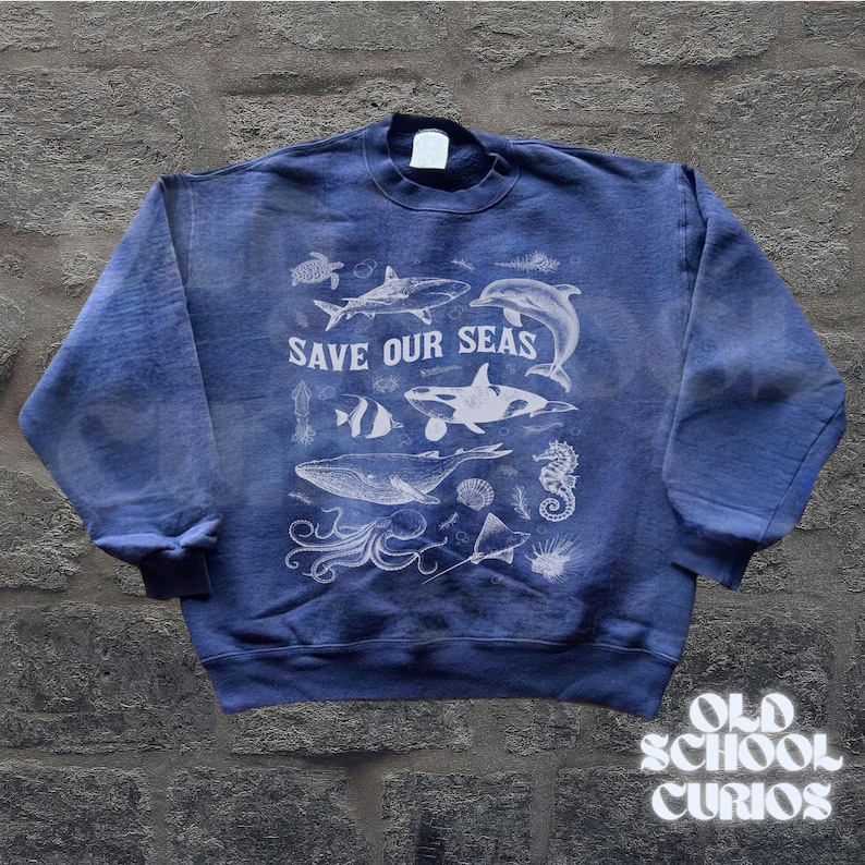 Puede incluir: Sudadera azul con un gr&aacute;fico blanco de varias criaturas marinas, incluyendo una ballena, un tibur&oacute;n y un delf&iacute;n. El texto "SAVE OUR SEAS" est&aacute; impreso encima de las criaturas marinas. La sudadera tiene cuello redondo y mangas largas.