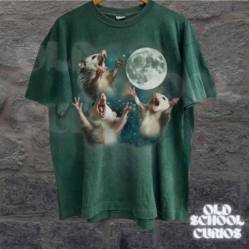 May include: Green t-shirt featuring a graphic of three opossums howling at a full moon against a starry background. The shirt has a vintage, faded look. The text "OLD SCHOOL CURIOS" is printed in white on the lower right.