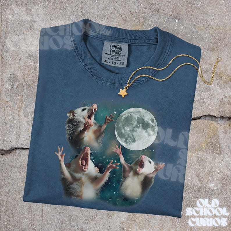 K&ouml;nnte beinhalten: Ein marineblaues T-Shirt mit einer Grafik von drei Opossums, die den Vollmond anheulen. Das Shirt hat einen Rundhalsausschnitt und kurze &Auml;rmel. Eine goldfarbene Sternanh&auml;nger-Halskette ist &uuml;ber dem Shirt drapiert. Der Text "Old School Curios" ist sichtbar.