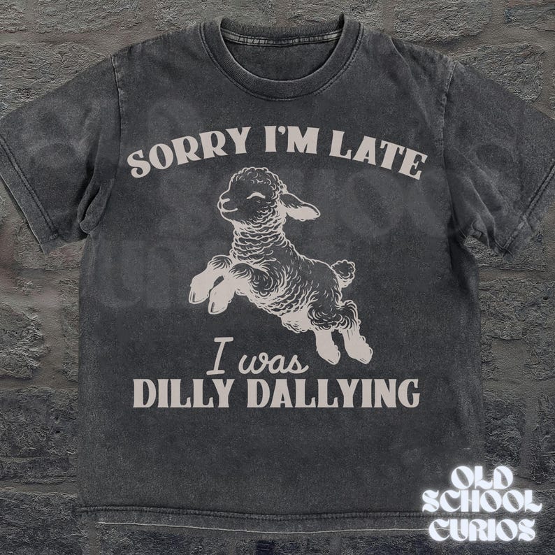 May include: Dark gray t-shirt with the text "SORRY I'M LATE I WAS DILLY DALLYING" and a graphic of a jumping lamb. The shirt has a vintage, distressed look. The brand "OLD SCHOOL CURIOS" is printed at the bottom right.
