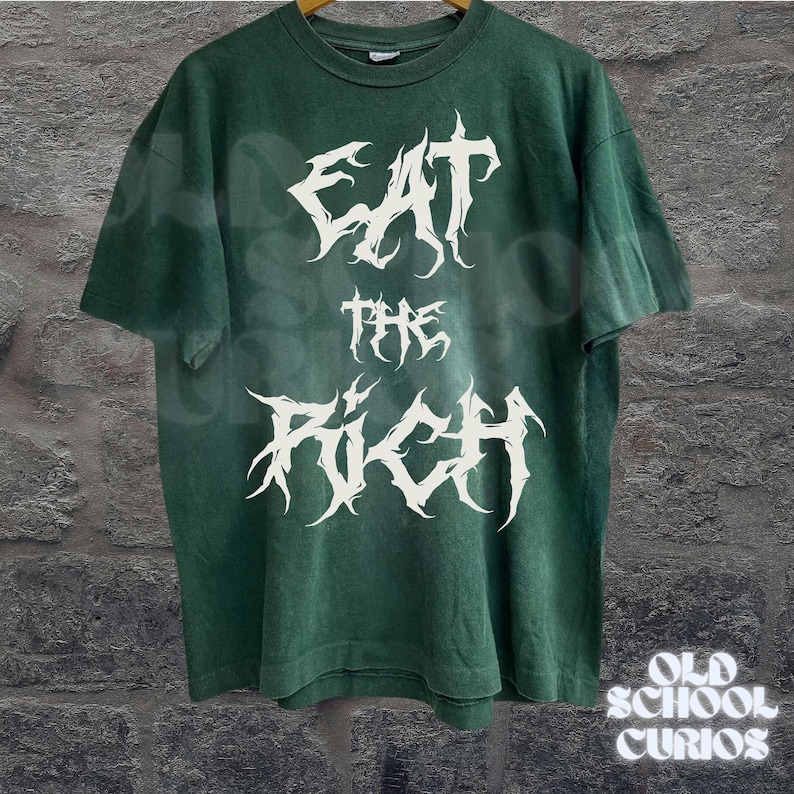 May include: Green t-shirt with the white text "EAT THE RICH" in a gothic font. The shirt has short sleeves and a crew neck. The words "OLD SCHOOL CURIOS" are in white text at the bottom right.